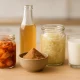 assorted fermented foods including kimchi, kefir, miso, sauerkraut, and kombucha on a light wooden table for gut health and probiotics benefits