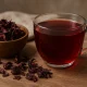 Glass cup of hibiscus tea with dried hibiscus flowers on rustic wooden table