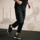 Man running in a gym setting during a Hyrox-style workout, with training equipment subtly in the background — dynamic fitness in motion.
