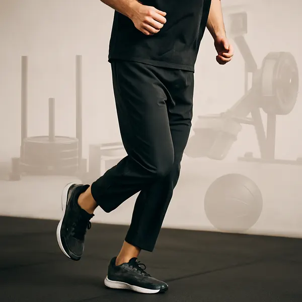 Man running in a gym setting during a Hyrox-style workout, with training equipment subtly in the background — dynamic fitness in motion.